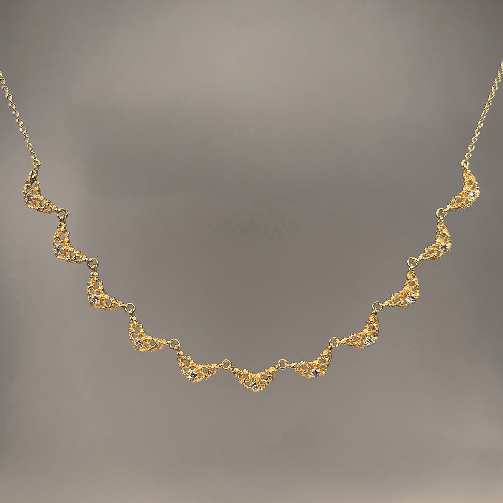 A necklace made up of 11 small, delicate, textured and lacy quarter-moon shaped pieces with 1 diamond in each, centered at the bottom; remainder of necklace is fine chain
