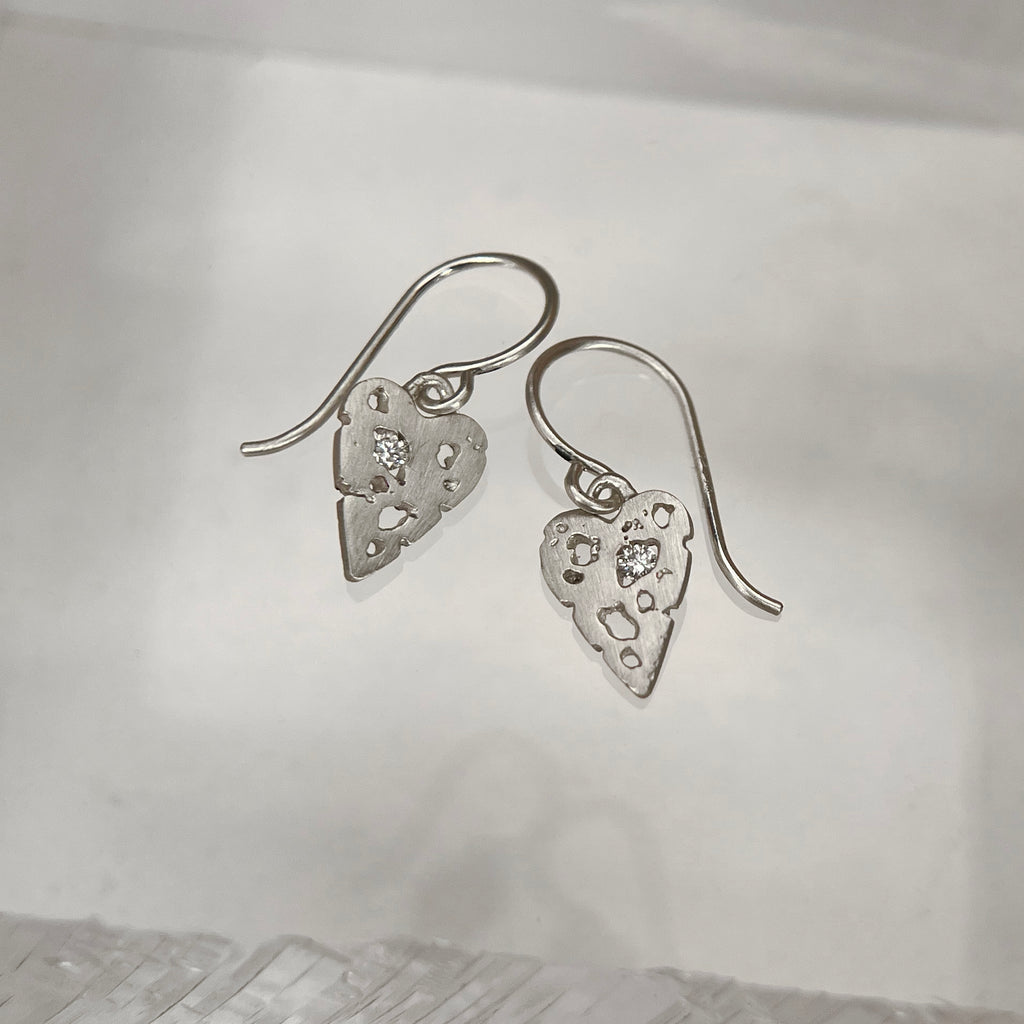 Flat but slightly thick heart with negative spaces, one of which holds a stone; shown in silver with diamonds