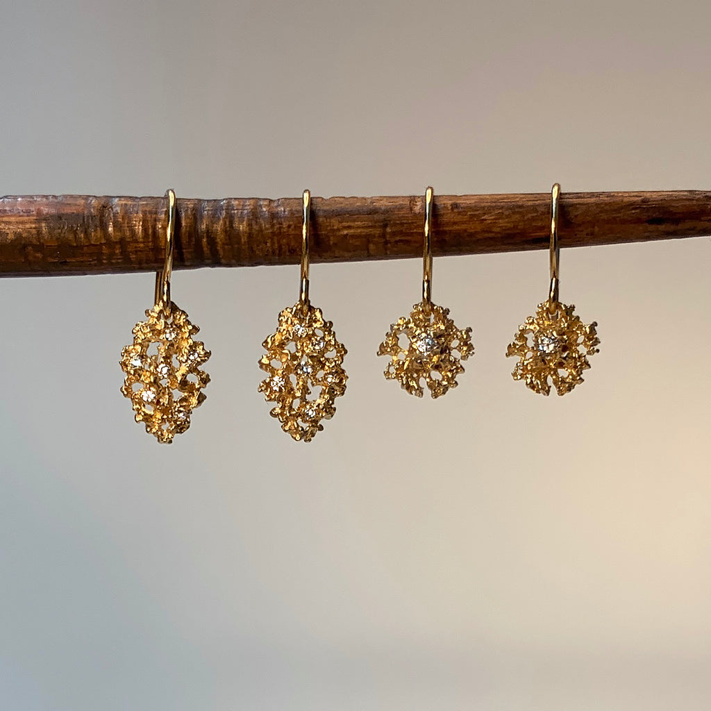 Two pairs of textured, lacy earrings hang from a rough chopstick, one leaf-shaped, one rounded; the leaf has 7 tiny diamonds and the round one has one larger diamond in the center