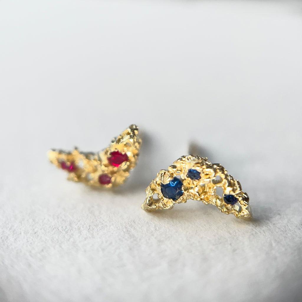 photo shows two small, textured, lacy studs, with 3 stones each, one with rubies, and one with blue sapphires