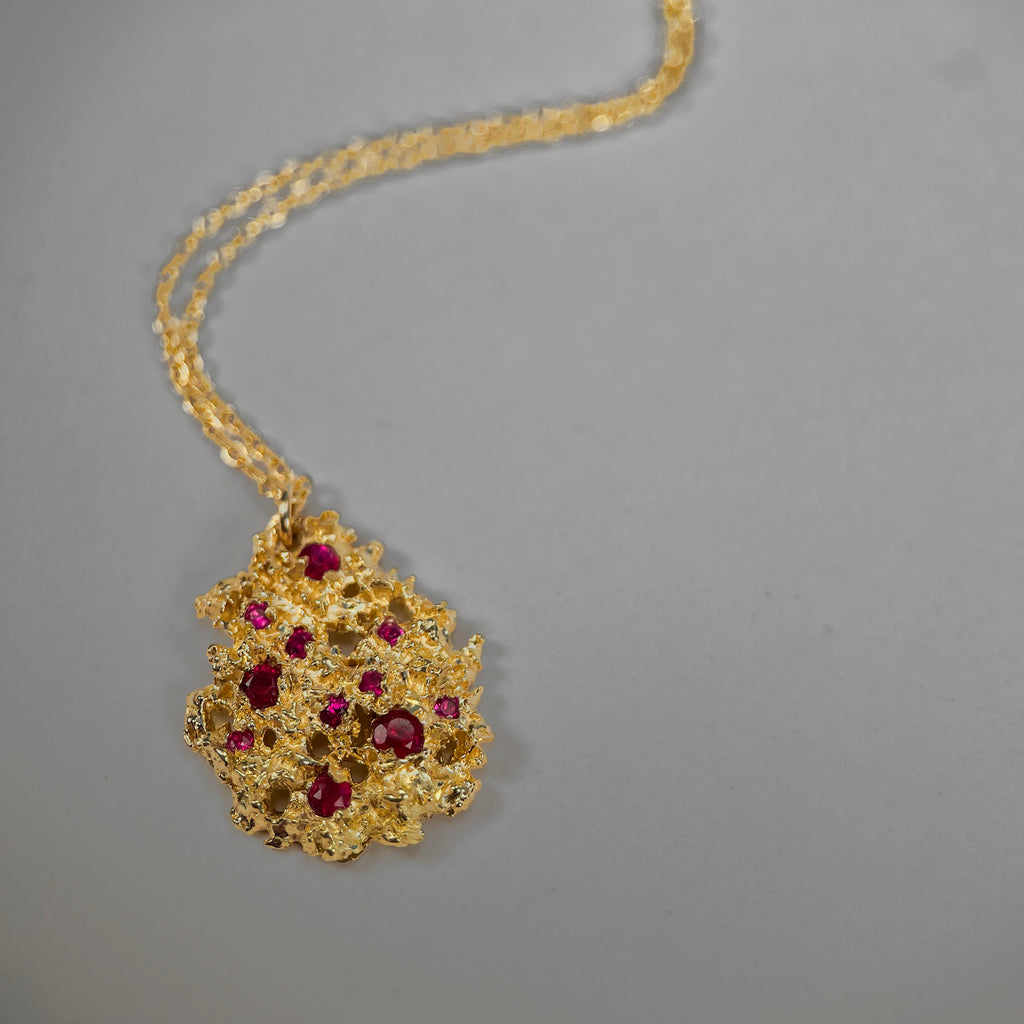 Textured, pear-shaped pendant shown in rich yellow 18k with 11 rubies of varying sizes