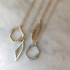 Hollow, open hexagon pendant with 4 diamond "buds" placed asymmetrically; shown in yellow gold and silver; shown with open trapezoid oendant with 3 diamond buds