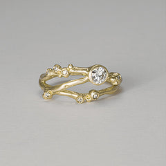 Organic, branch-like ring with three branches. Large off-center stone and seven tiny diamond buds. Shown in yellow gold. Front view.