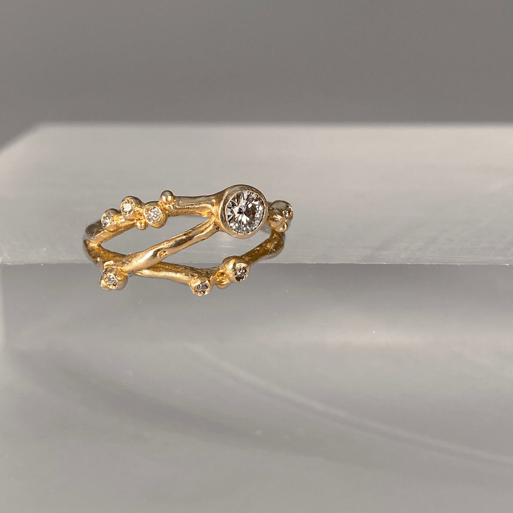 Organic, branch-like ring with three branches. Large off-center stone and seven tiny diamond buds. Shown in yellow gold. Angled view.