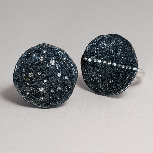 two textured, round rings shown, in blackened silver, one with a stripe of diamonds up and down, and the other with scattered diamonds
