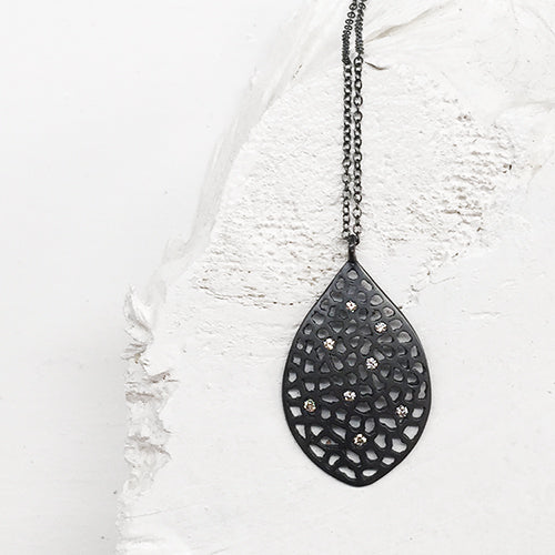 leaf-shaped, slightly convex pendant; has 8 white diamonds scattered over the piece; overall pattern made by organic cutouts; shown in blackened silver 