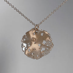 round ruffled pendant with textured edges and jagged holes and 1 white diamond; shown in silver