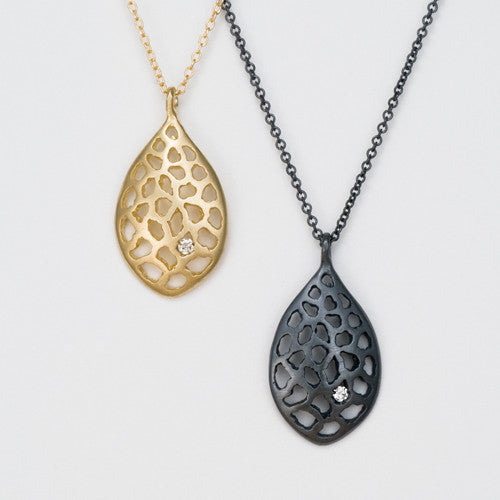 A leaf-shaped pendant with lacy negative space; shown in blackened silver and yellow gold, with 1 diamond set in a hole in the lower right