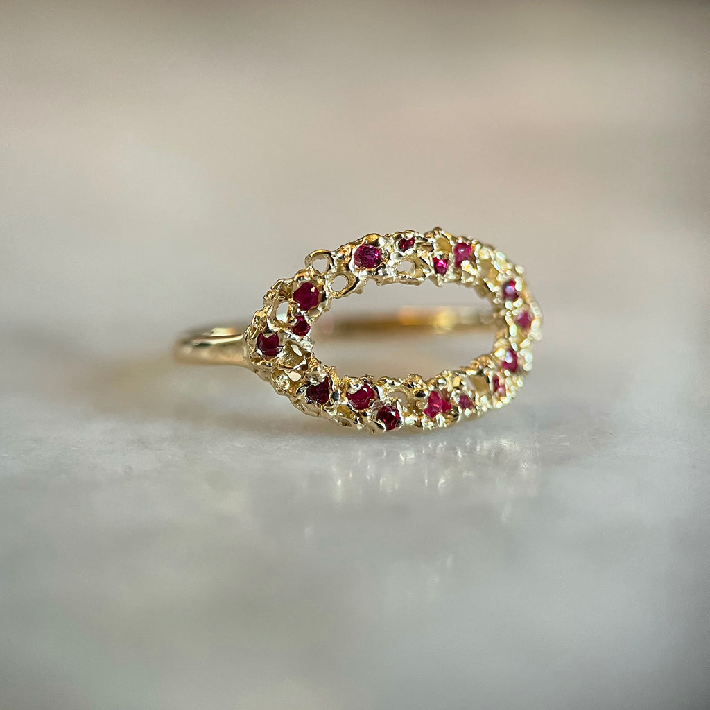 A light and airy gold ring; lacy with organic holes; shown with scattered tiny rubies of various sizes