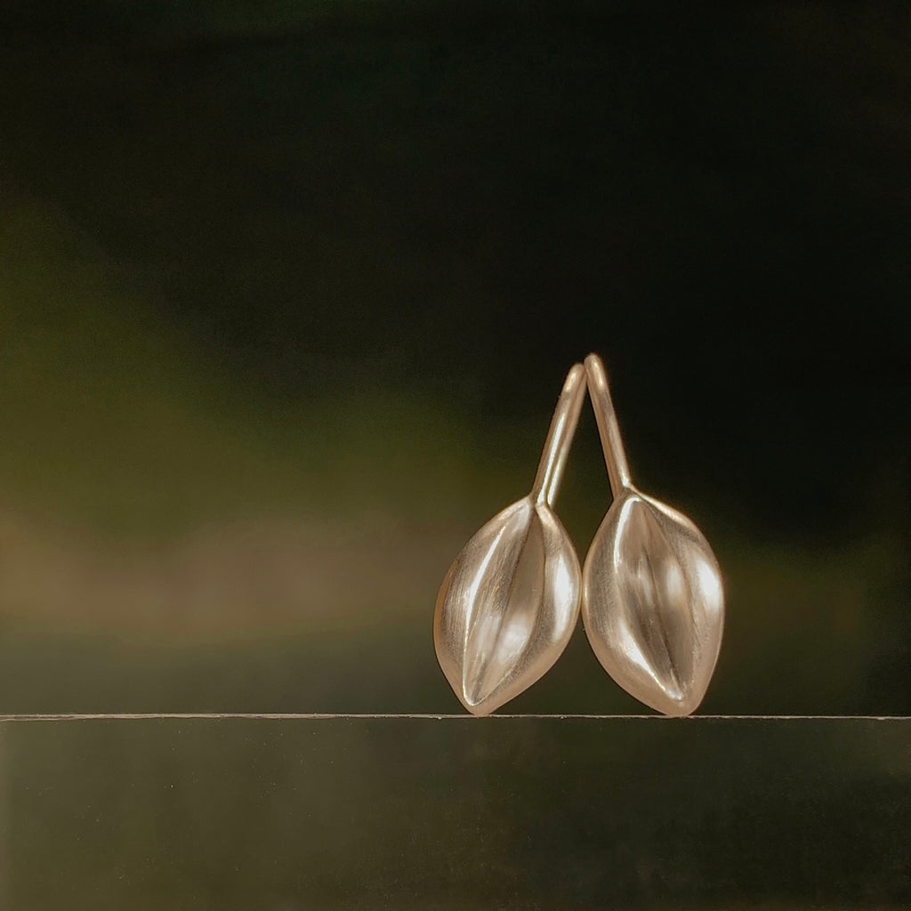 a pair of magnolia fruit-shaped earrings, shown in silver, stand upright against a dark green background