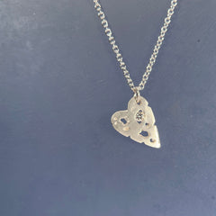 flat, small heart with organic cutouts, one of which holds a stone, hanging from a corner; shown here in silver with a white diamond and a satin finish