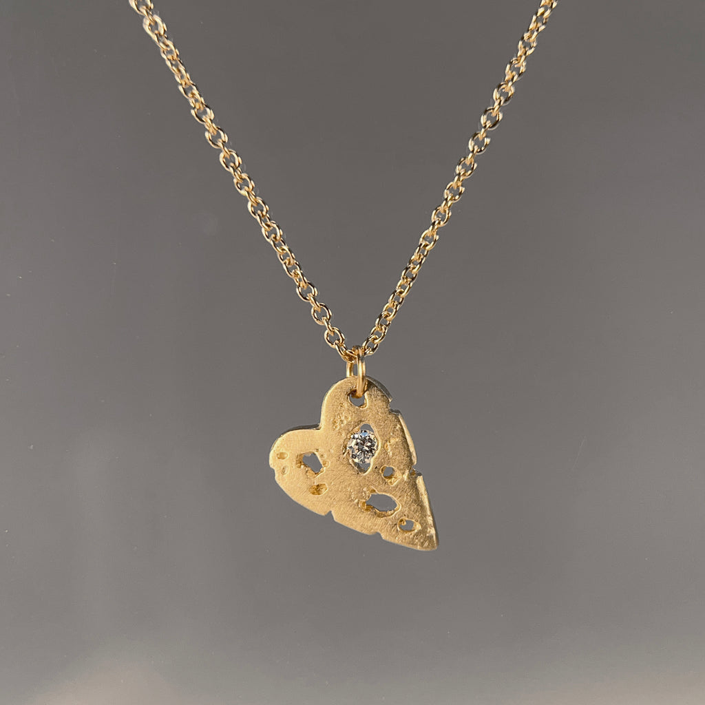 flat, small heart with organic cutouts, one of which holds a stone, hanging from a corner; shown here in yellow gold with a white diamond and a satin finish