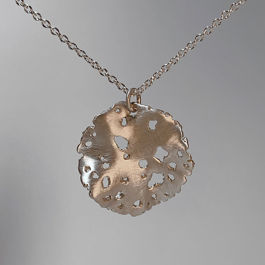 A wavy, circular pendant with a rough, irregular edge and rough cutouts scattered throughout