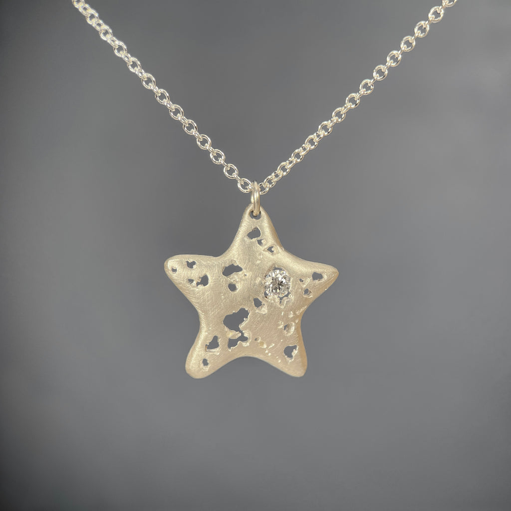 starfish-shaped pendant with soft edges, jagged holes, and 1 white, off-center diamond; shown in silver