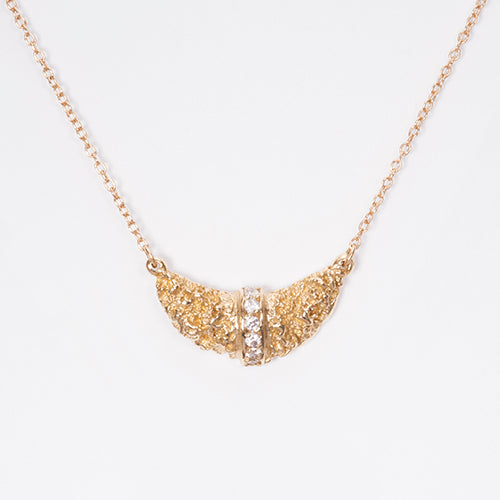 Textured, croissant-shaped necklace hangs sideways; diamond stripe bissects croissant