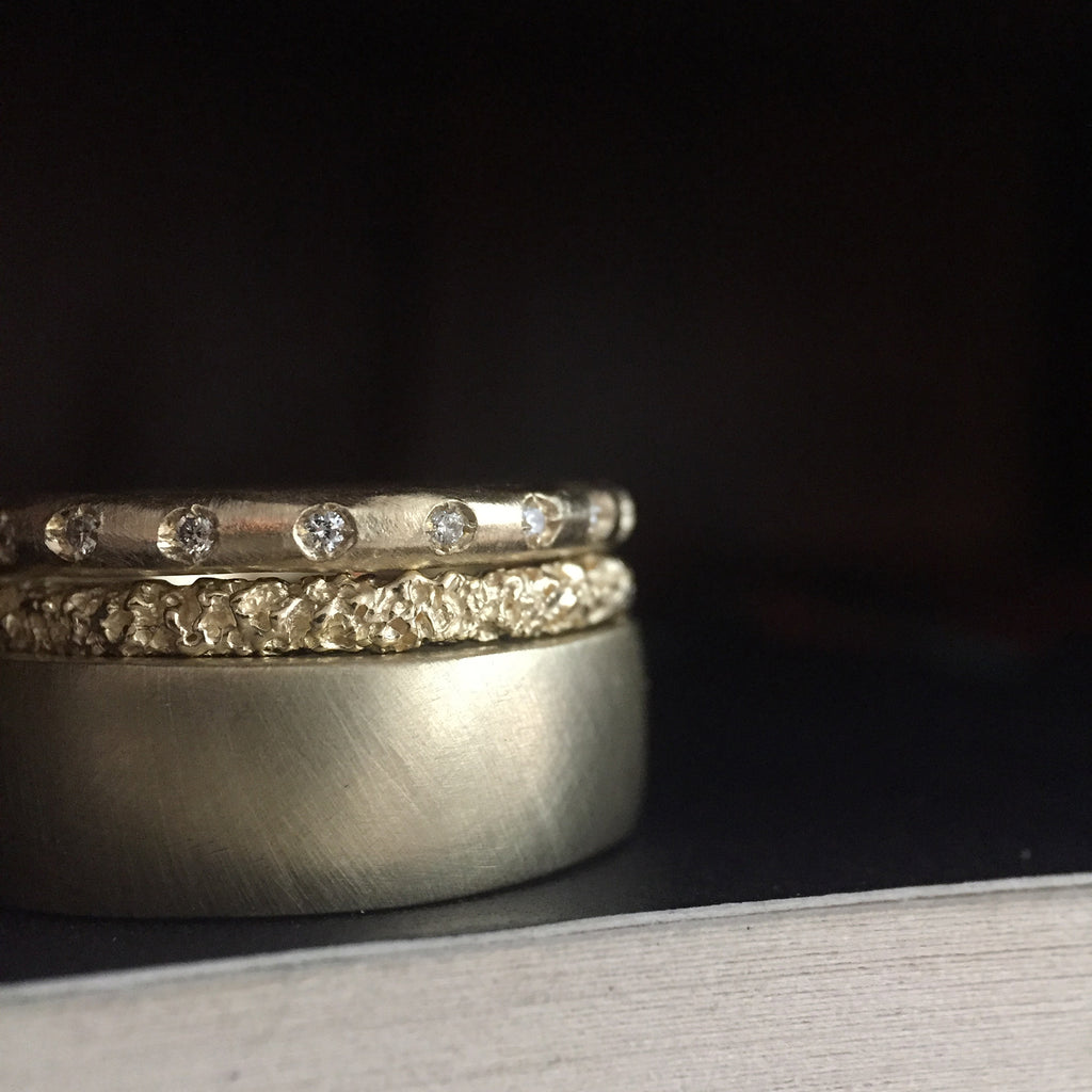 medium width band with squared-off-edges, shown stacked with slim, textured, domed band and rounded band set with diamonds