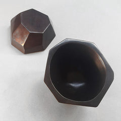 Asymmetrical bowl with large facets on outside and round smooth inside; tilts slightly; heavy cast bronze; shown in black, top and bottom
