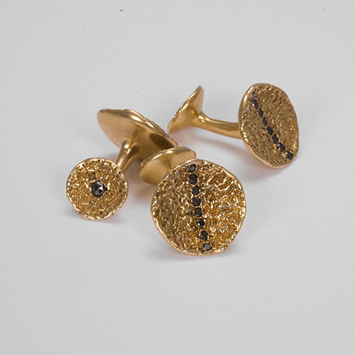 Cufflinks with larger concave round main element bissected by stripe of black diamonds, and smaller concave element with single black diamond in center