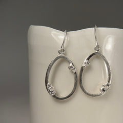 Hollow, open oval with 3 diamond "buds" placed asymmetrically; shown in silver; wire earring