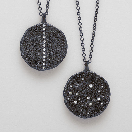 two textured, round pendants shown, in blackened silver, one with a stripe of diamonds up and down, and the other with scattered diamonds