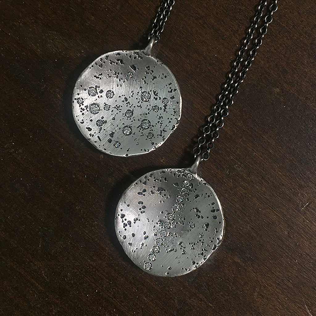 two textured, round pendants shown, in slightly blackened silver, one with a stripe of diamonds up and down, and the other with scattered diamonds