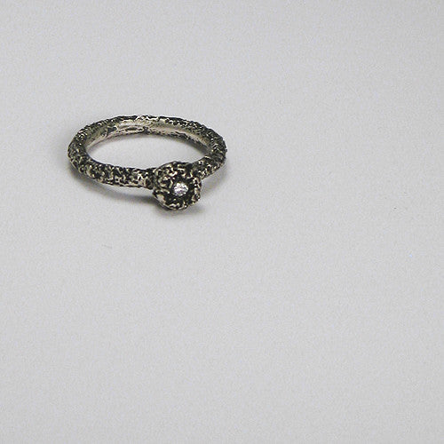 Round, textured band with donut-like pod on top, and whiet diamond in center of pod; blackened in crevices