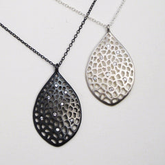 leaf-shaped, slightly convex pendant; has 8 white diamonds scattered over the piece; overall pattern made by organic cutouts; shown in blackened and satin silver 