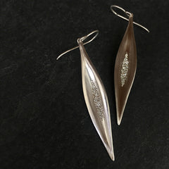 Slender, elongated, concave leaf shape base on a pod from the fruit of a magnolia tree; set with cluster of diamonds in various sizes in center; shown in matte silver
