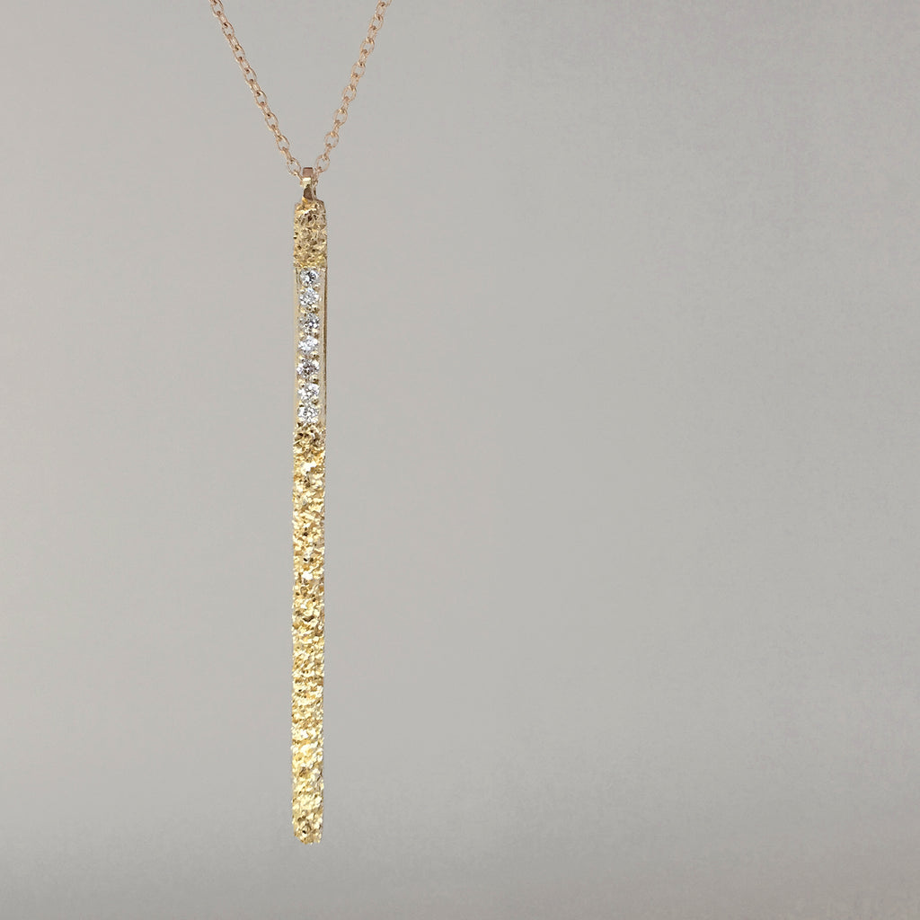Long, thin, vertical, textured stick, interrupted by row of pavé set white diamonds in top 1/3; shown in yellow gold
