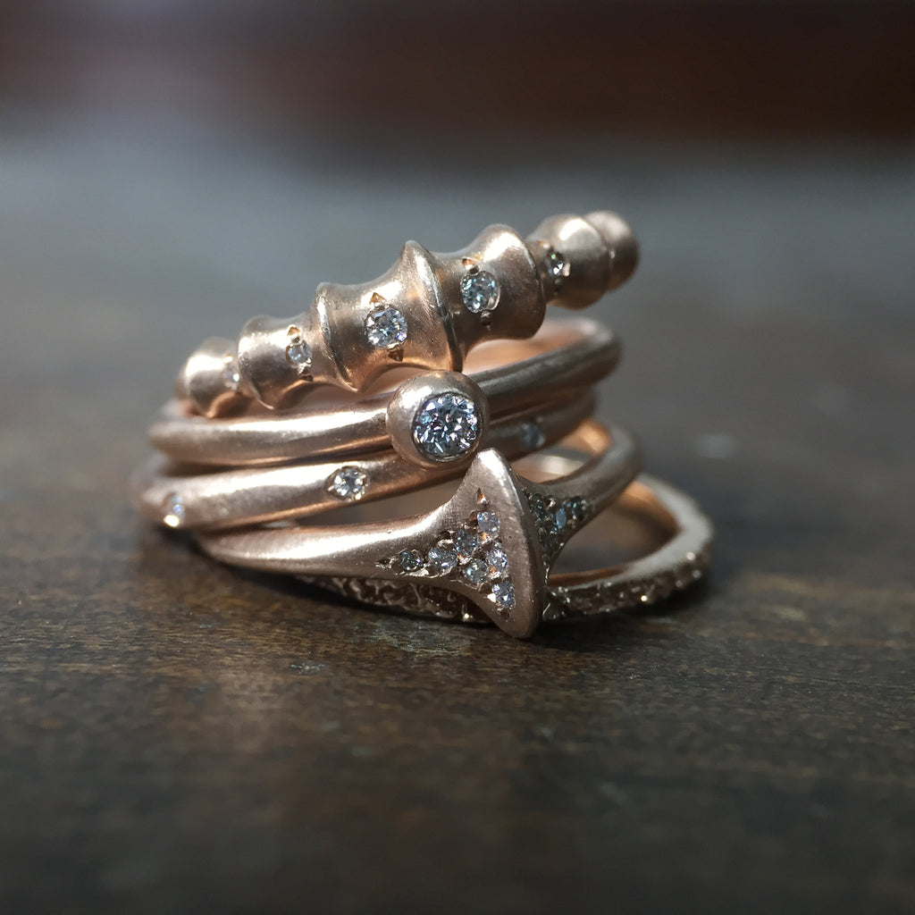 Ridged band at top of stack; raised portions travel around the top half of the band; diamonds set in each low portion; followed by 4 other rose gold diamond bands