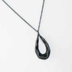 Teardrop-shaped pendant with negative space in center and ruffle following shape around; shown in blackened silver