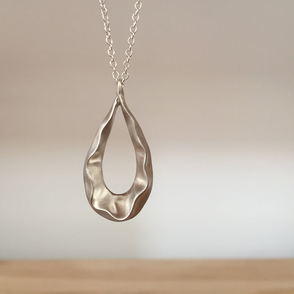 Teardrop-shaped pendant with negative space in center and ruffle following shape around; shown in satin silver