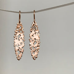 Shiny ellipse-shaped earring on wire, with organic holes, shown in rose gold.