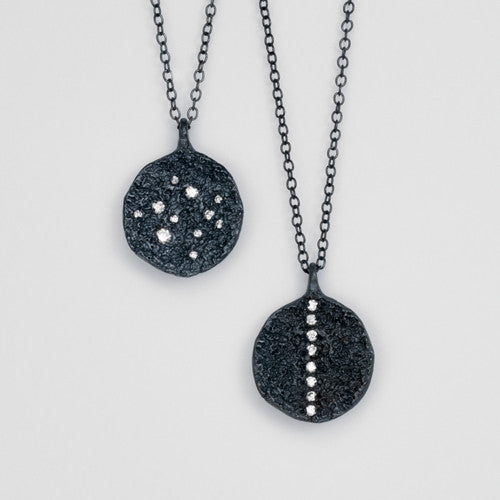 two textured, round pendants shown, in blackened silver, one with a stripe of diamonds up and down, and the other with scattered diamonds