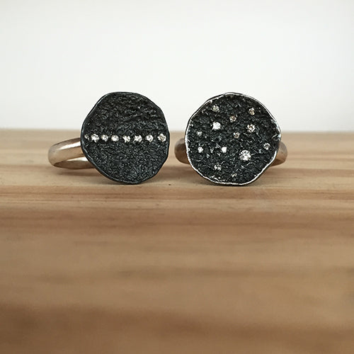two rings with textured, round concave domes shown, in blackened silver, one with a stripe of diamonds up and down, and the other with scattered diamonds