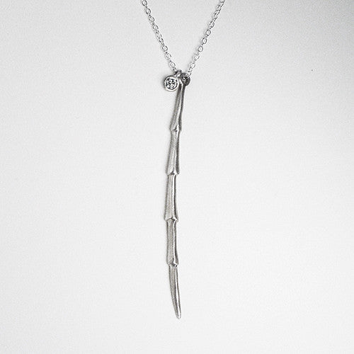 Long, skinny pendant with 5 sculpted elements has diamond solitaire nestled next to it