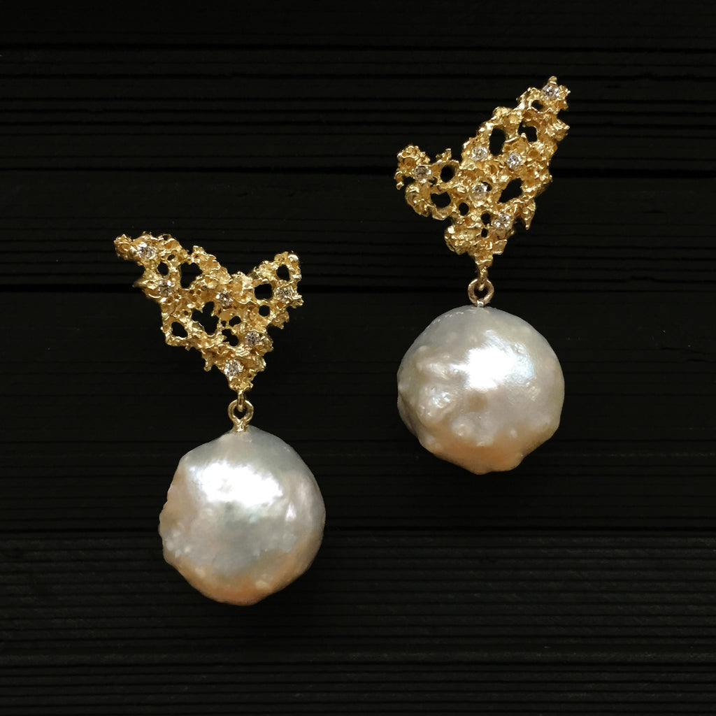 Organic, uneven, and bumpy pearls hang from wing-like element, which is textured, lacy, and studded with diamonds