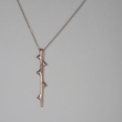 Stylized branch with 5 thorns, 3 on one side and 2 on the other, each with a diamond in the center; hangs vertically; shown in rose gold