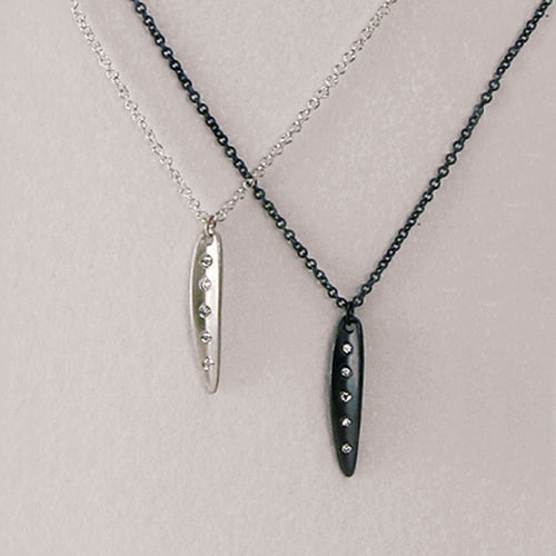 Very small, narrow leaf pendant; shape is slightly convex with vertical crease in center; shown in silver and blackened silver; 5 diamonds follow the crease